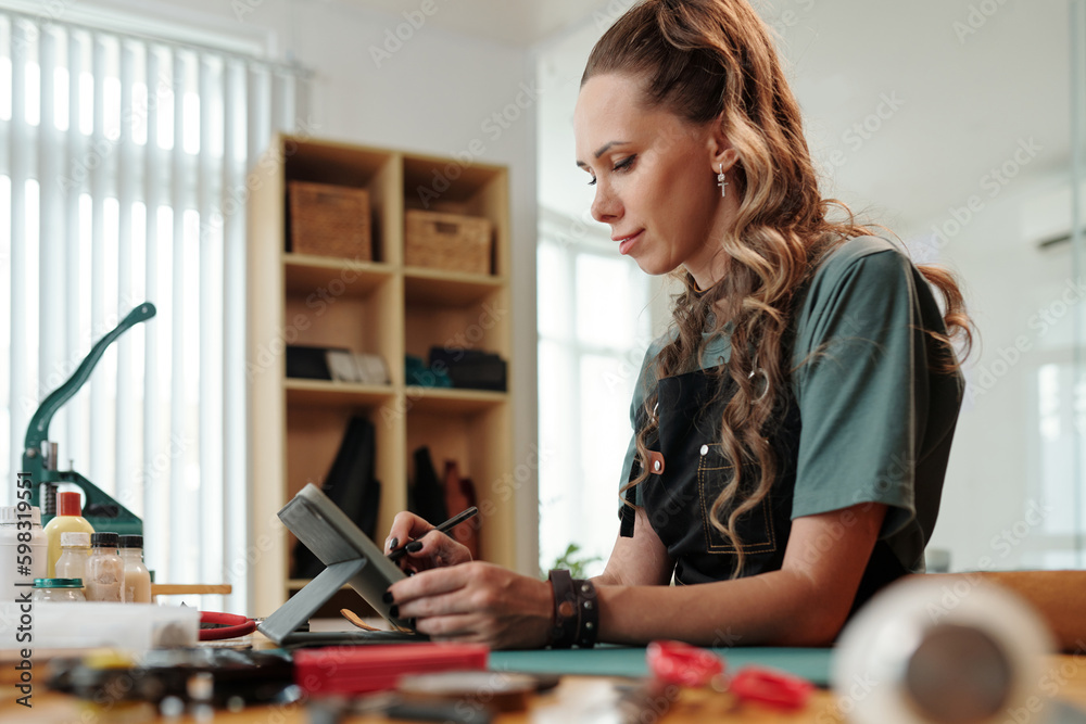 Fototapeta premium Cheerful young woman drawing sketch of leather belt on tablet computer