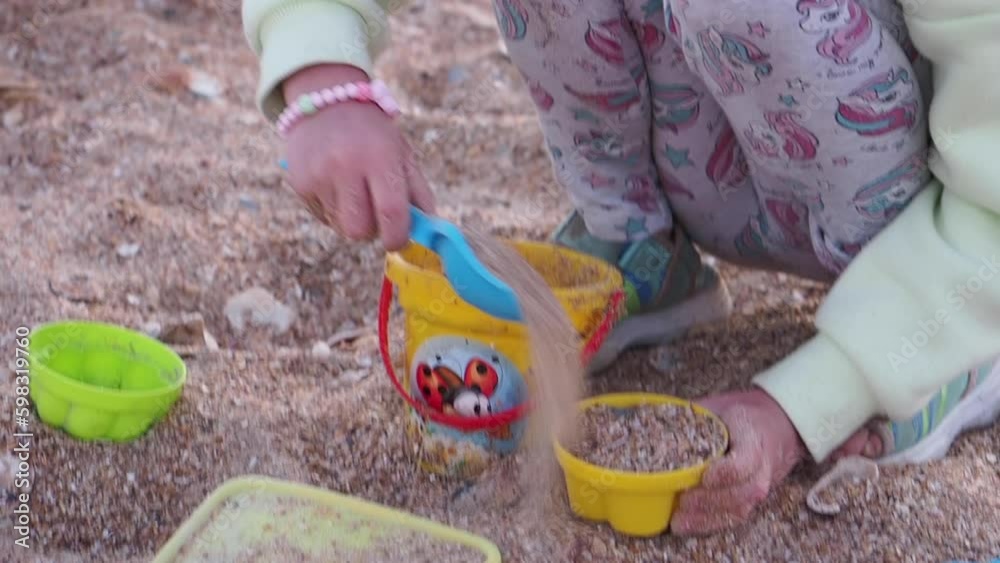 Girl playing with sand and bucket on the beach. Colored toy shapes. Sunset Girl playing with sand and bucket on the beach. Colored toy shapes. Sunset