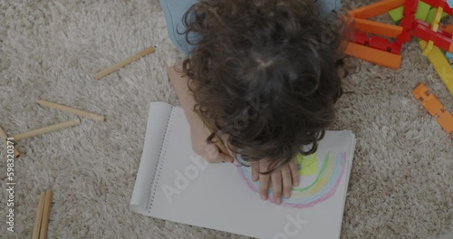 Top view of cute little boy drawing colorful picture with rainbow sitting on carpet at home. Creative children and craftswork concept. Generative AI photo