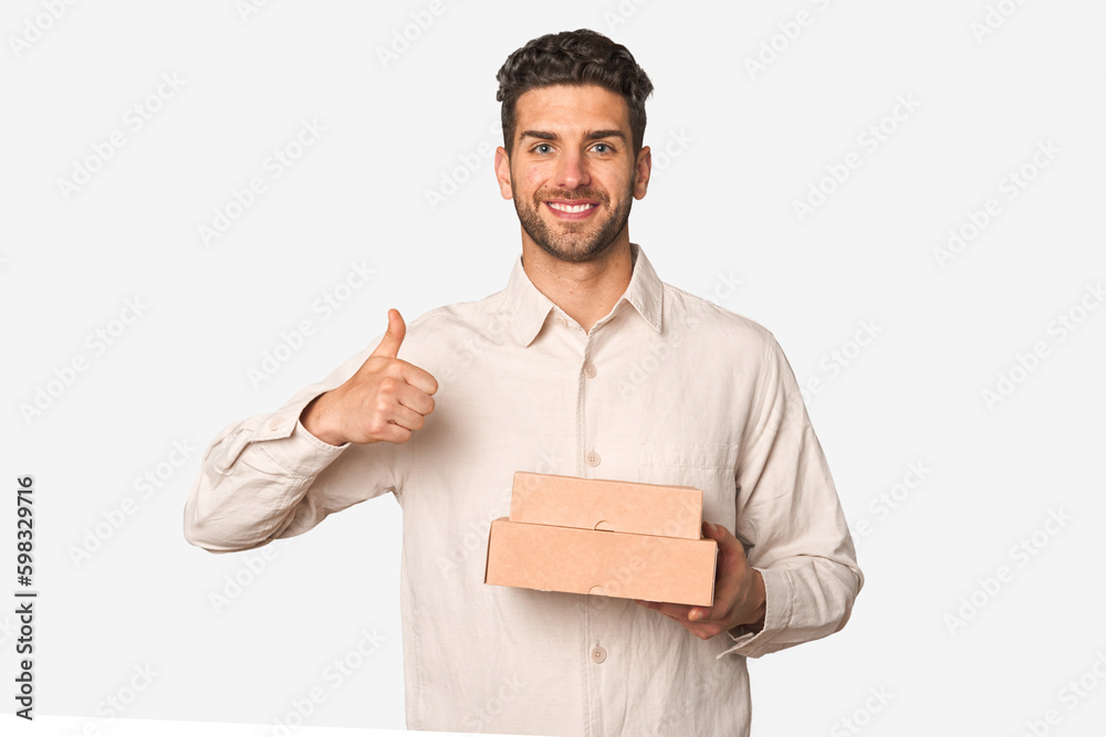 Young man holding a takeaway boxes isolated smiling and raising thumb up Young man holding a takeaway boxes isolated smiling and raising thumb up