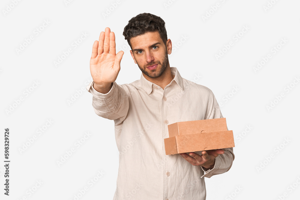 Young man holding a takeaway boxes isolated standing with outstretched hand showing stop sign, preventing you. Young man holding a takeaway boxes isolated standing with outstretched hand showing stop sign, preventing you.