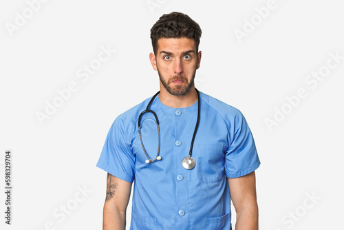 Young nurse man shrugs shoulders and open eyes confused.