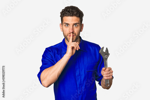 Young mechanic man holding a wrench keeping a secret or asking for silence.