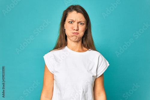 A young caucasian woman isolated blows cheeks, has tired expression. Facial expression concept.