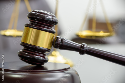 Legal office of lawyers, justice and law concept : Wooden judge gavel or a wood hammer and a soundboard used by a judge person on a desk in a courtroom with a blurred brass scales of justice behind. photo