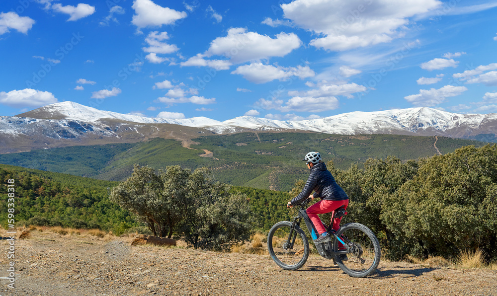 nice, active senior woman cycling with her electric mountain bike below the snow covered mountains of the Spanish Sierra Nevada, near Granada, Anslusia, Spain