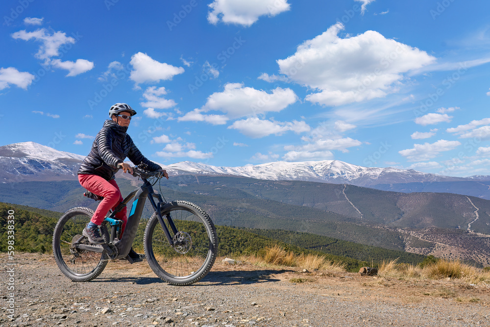 nice, active senior woman cycling with her electric mountain bike below the snow covered mountains of the Spanish Sierra Nevada, near Granada, Anslusia, Spain nice, active senior woman cycling with her electric mountain bike below the snow covered mountains of the Spanish Sierra Nevada, near Granada, Anslusia, Spain