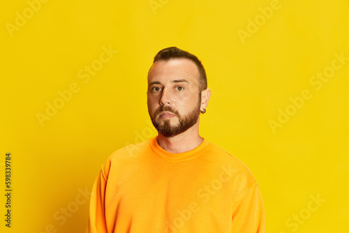 Portrait of bearded man with short hair, wearing sweatshirt and seriously looking at camera against vivid yellow background. Concept of human emotions, lifestyle, facial expression. Ad