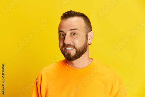 Portrait of young bearded man with short hair looking at camera, posing against vivid yellow background. Concept of human emotions, lifestyle, facial expression, fashion, sales, news. Ad