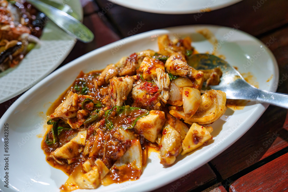 Stir fried chicken meat with chili paste sauce and herbs in white plate