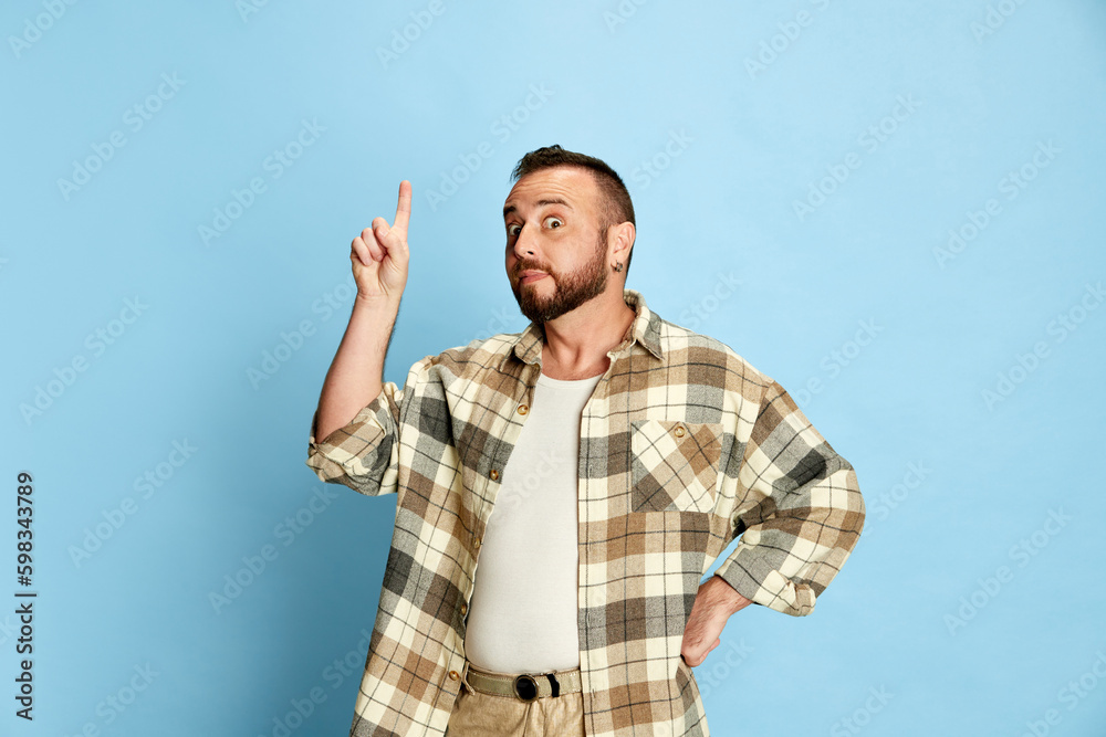 Portrait of bearded man in casual clothes, checkered shirt raising finger up, expressing ideas against blue studio background. Concept of human emotions, lifestyle, facial expression. Ad Portrait of bearded man in casual clothes, checkered shirt raising finger up, expressing ideas against blue studio background. Concept of human emotions, lifestyle, facial expression. Ad
