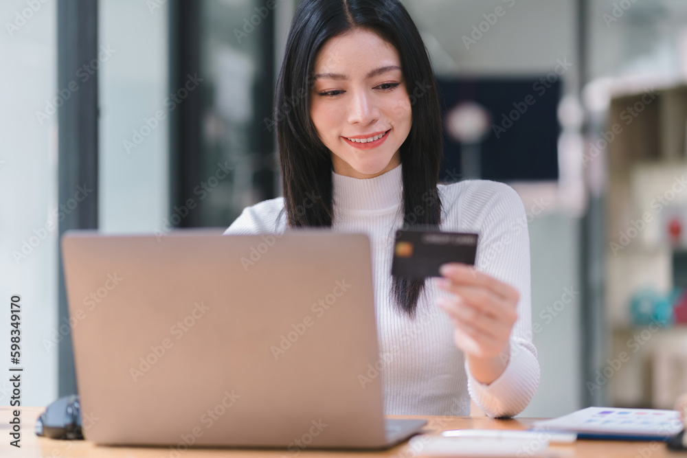 Cropped shot of female using laptop and hand holding black credit card mockup at workplace. Selective focusing