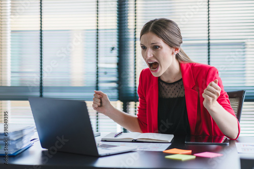 Murais de parede A stressed and frustrated businesswoman is seen sitting at her desk, shouting at her laptop in anger due to a mistake or crisis in the business
