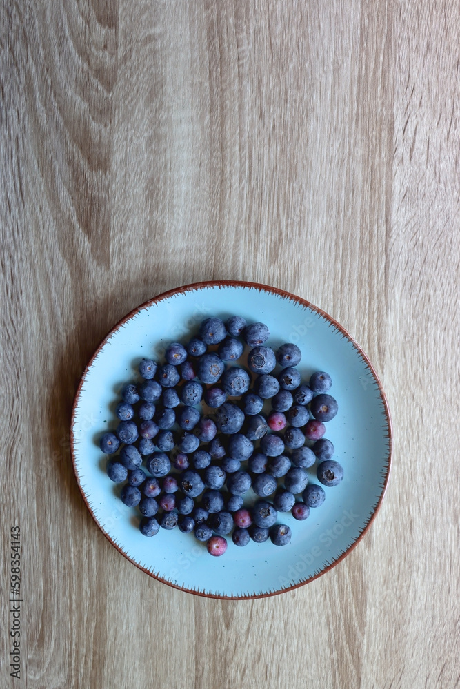 Turquoise plate with fresh blueberries on wooden background. Top view.