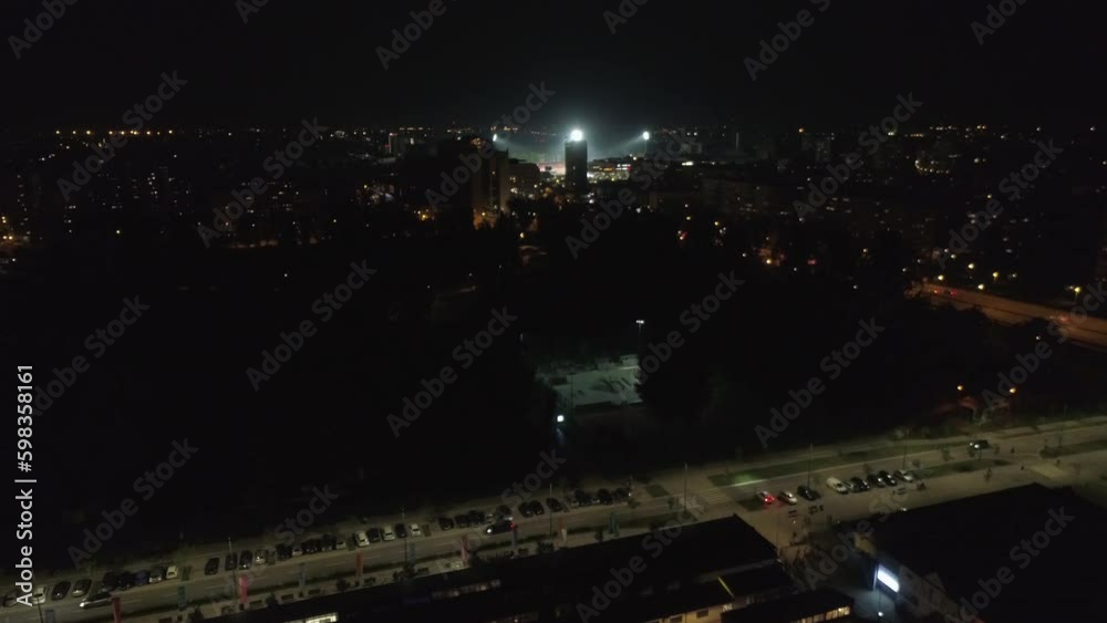 Drone night flight over a street town city cars light. Aerial night shot. Flying over a road towards a football stadium. City road lights cars passing. Drone night flight over a street town city cars light. Aerial night shot. Flying over a road towards a football stadium. City road lights cars passing.