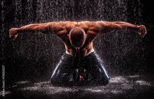 Athlete bodybuilder under jets of rain on a black background