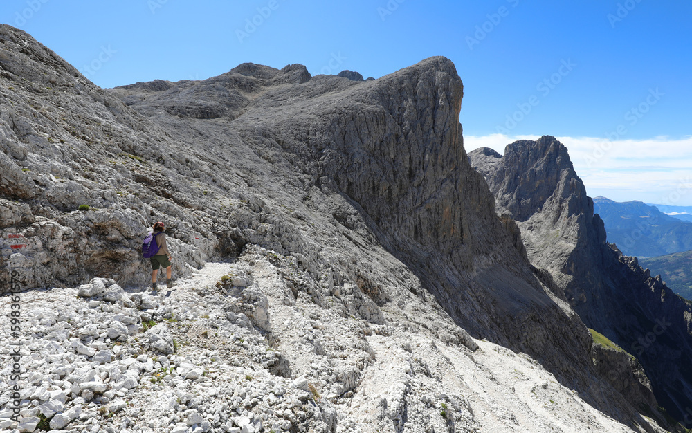 young woman walks with backpack on the path of dolomite alps in northern italy