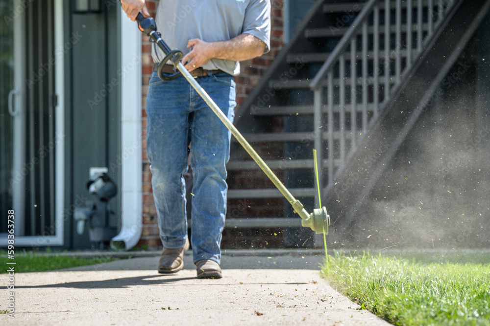 lawn care worker trimming grass along side walk with weed eater