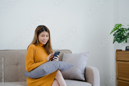 Asian girl using cell phone for checking social media at home holding smartphone in morning
