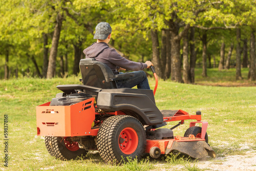A young teenage boy is riding a zero turn lawn mower and using it to mow.