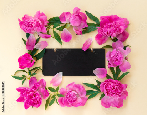 Garland of beautiful pink peonies on yellow paper background with wooden desk for congratulations or invitations. Creative floral wreath. Greeting card for holiday.