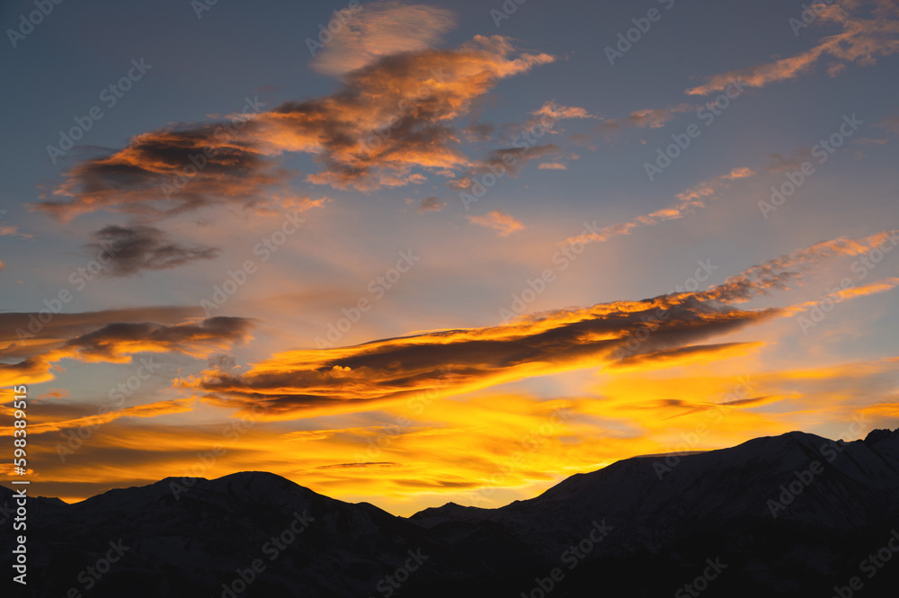 Colorful sunset over mountain hills. The black silhouette of the mountains is visible through the picturesque glow