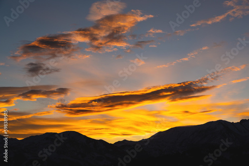 Colorful sunset over mountain hills. The black silhouette of the mountains is visible through the picturesque glow