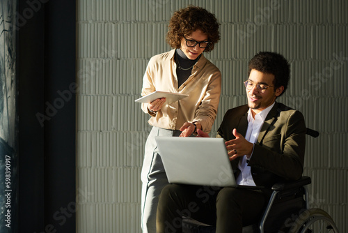 Two young intercultural brokers discussing online data on laptop screen while preparing presentation of new project for conference photo