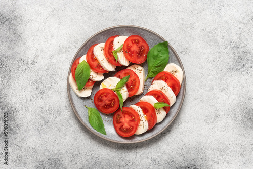 Caprese salad. Italian salad with chopped tomatoes, mozzarella, basil, olive oil on a light stone background. Top view, flat lay