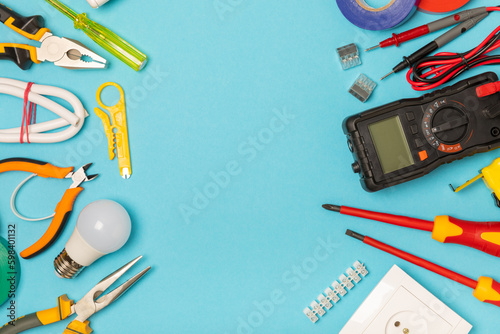 Electrician equipment on blue background with copy space.Top view.Electrician tool set.Multimeter, tester,screwdrivers,cutters,duct tape,lamps,tape measure and wires.Flet lay.