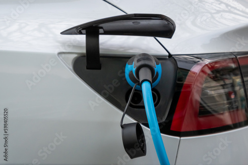 Ein weißes Elektro Auto hängt an der Ladesäule - Strom tanken mit Stecker in der Tanköffnung des Fahrzeugs