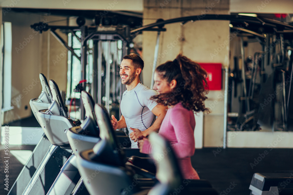 A fit sporty couple is running together on a treadmill in a gym during cardio training. - obrazy, fototapety, plakaty 