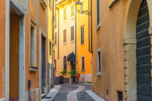 Fototapeta Naklejka Na Ścianę i Meble -  Medieval narrow paving stone street with yellowl buildings in Verona town, Veneto, Italy, Empty Italian street in old town