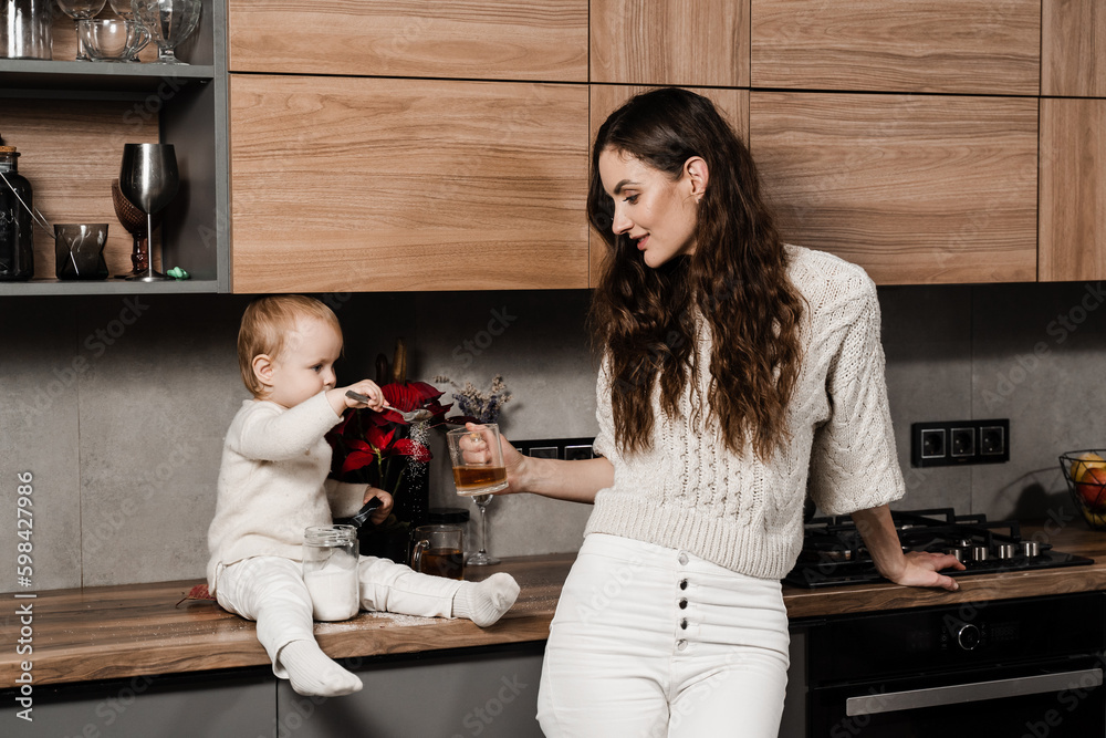 Mother and child daughter are drinking cup of tea on the kitchen. Maternity. Mon and her kid spend time at home together.