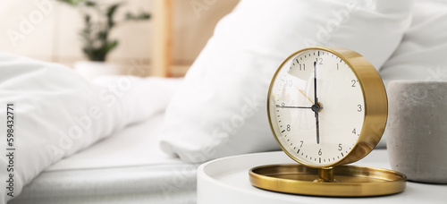 Stylish alarm clock on table in bedroom