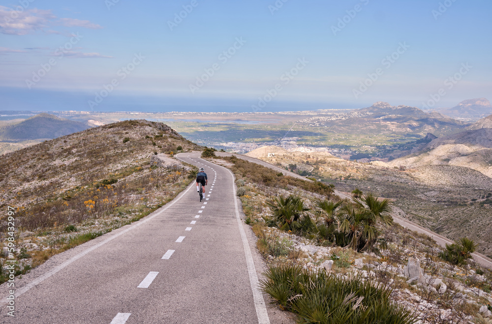 Cycling with beautiful mountains a sea view.A cyclist in full cycling gear and helmet is training on a road bike on an empty city road in sunny Spain.