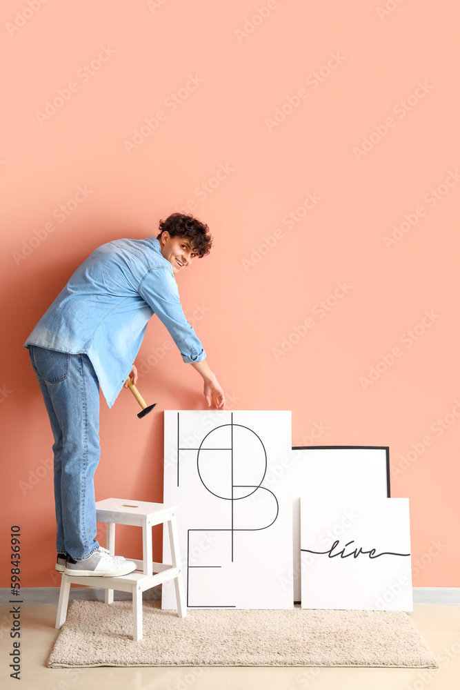 Young man hanging posters on pink wall