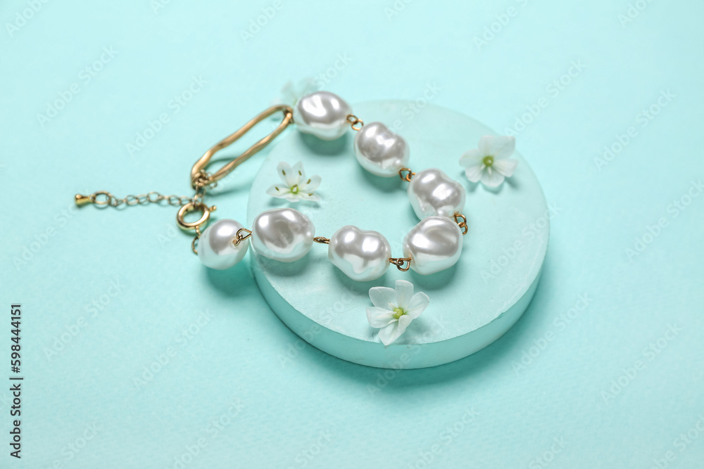 Showcase pedestal with pearl bracelet and flowers on blue background Showcase pedestal with pearl bracelet and flowers on blue background