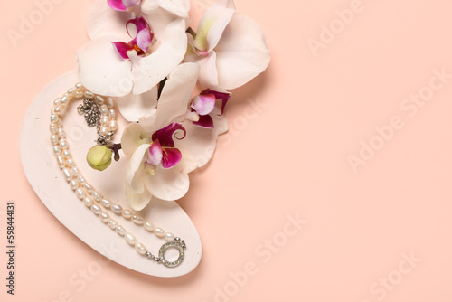 Showcase pedestal with pearl necklace and orchid flowers on pink background