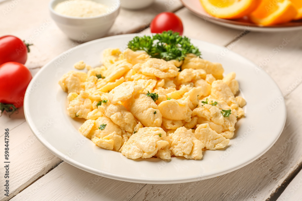Plate of delicious scrambled eggs with ingredients on white wooden background Plate of delicious scrambled eggs with ingredients on white wooden background
