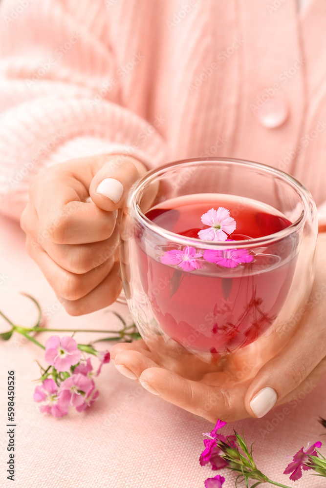 Female hands with cup of tea and delicate flowers on pink table Female hands with cup of tea and delicate flowers on pink table