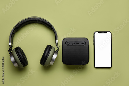 Wireless headphones, portable speaker and mobile phone on green background