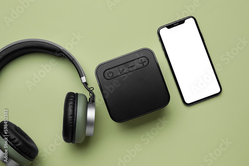 Wireless headphones, portable speaker and mobile phone on green background
