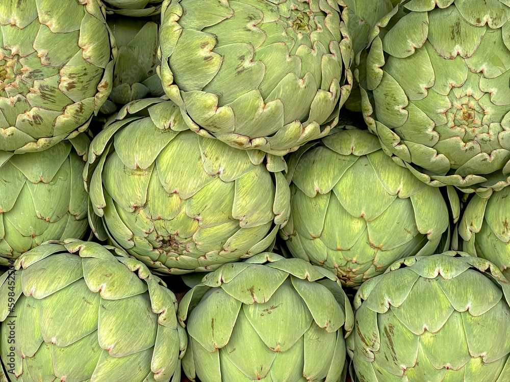Obraz premium Staked of raw Artichoke in market stall with selective focus, Fresh vegetable in wicker basket, The globe french artichoke is a variety of a species of thistle cultivated as a food.