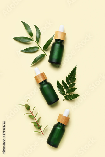 Bottles of cosmetic oil with plant twigs on beige background