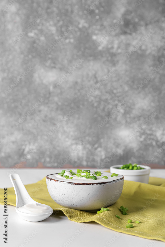 Bowl with sour cream and sliced green onion on white table near grunge wall Bowl with sour cream and sliced green onion on white table near grunge wall