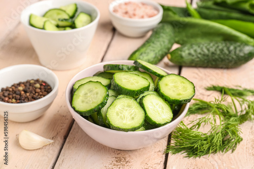 Bowl with pieces of fresh cucumber on light wooden background