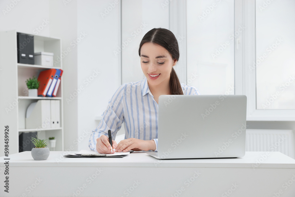 Young female intern working with laptop at table in office Young female intern working with laptop at table in office
