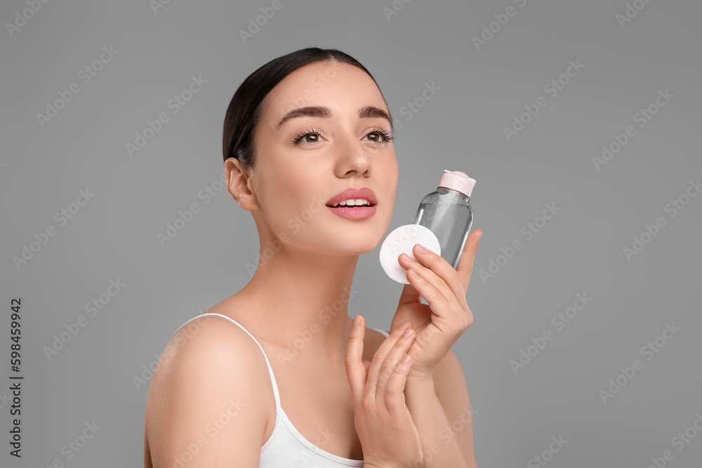 Beautiful woman with makeup remover and cotton pad on gray background Beautiful woman with makeup remover and cotton pad on gray background
