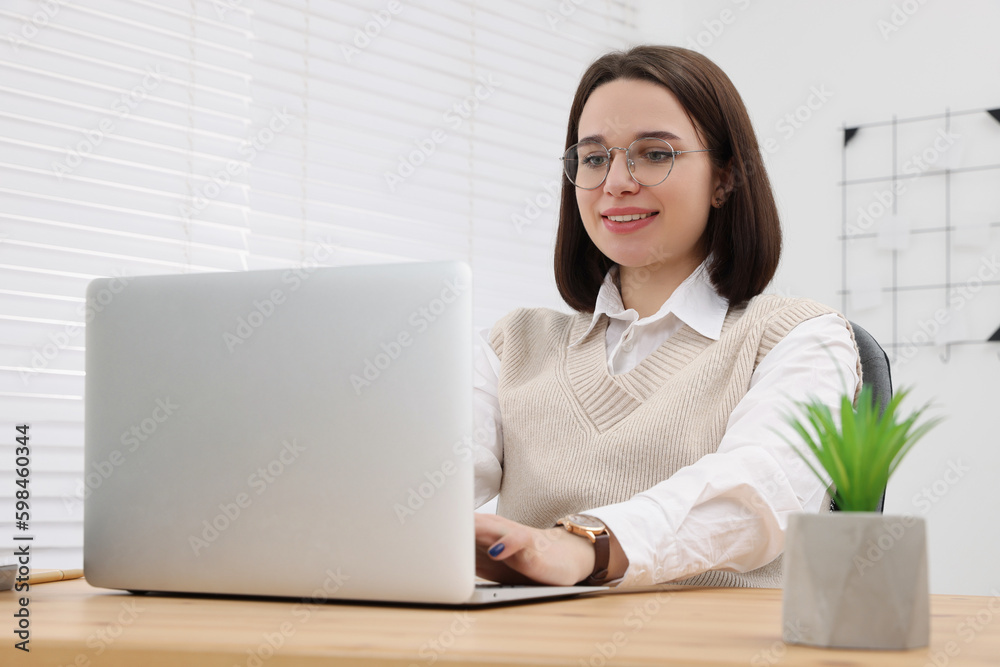 Happy young intern working with laptop at table in modern office Happy young intern working with laptop at table in modern office